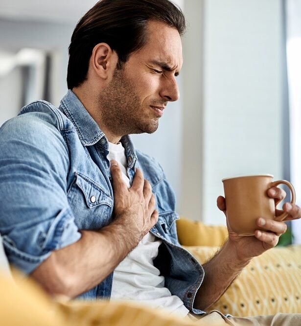 Man experiencing chest pain while sitting on a sofa, representing heart attack symptoms and urgent care by Dr. Akhilesh Jain for Heart Attack Treatment in Indore.